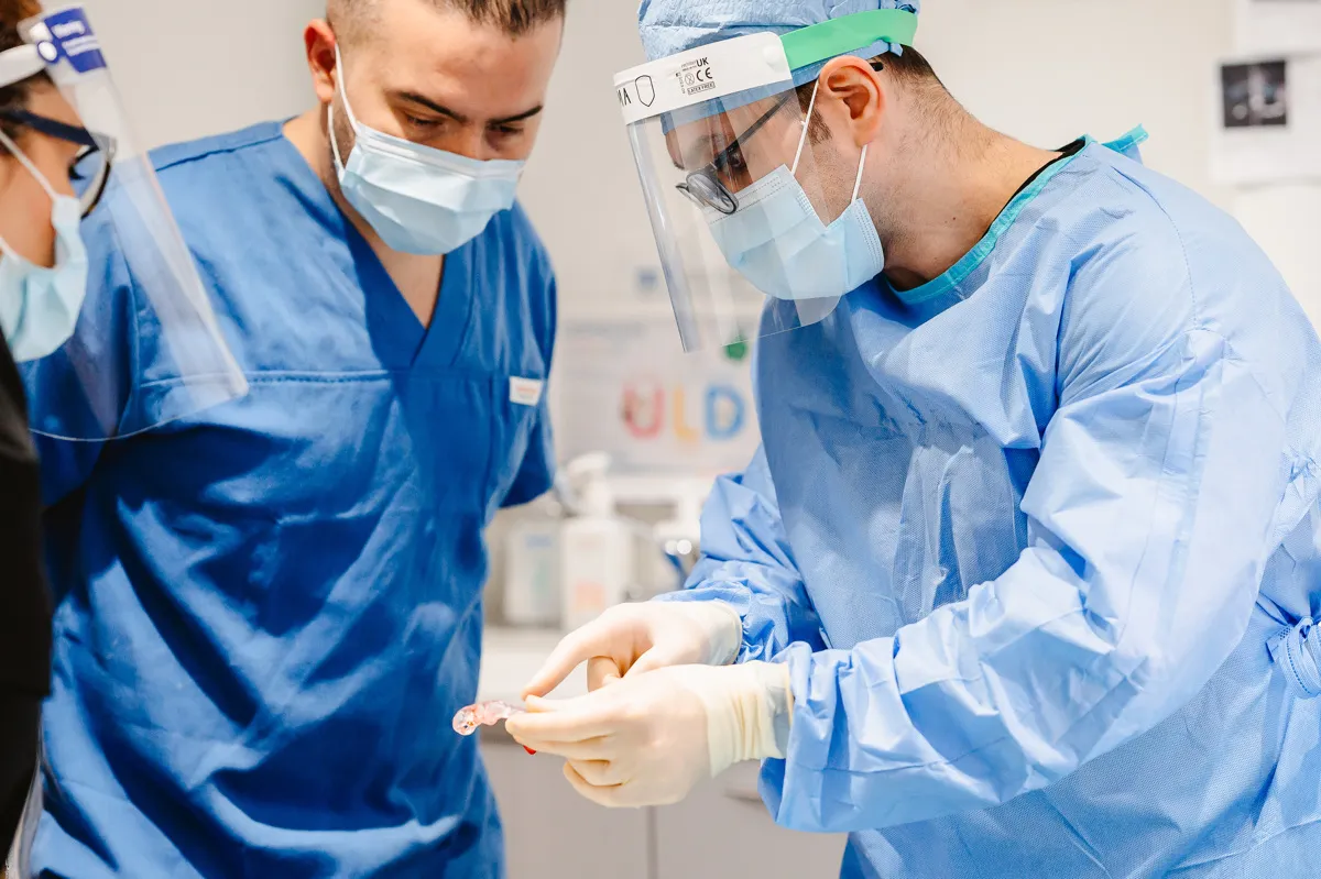 Two medical professionals in blue scrubs and face masks examining a dental mold in a clinical setting.