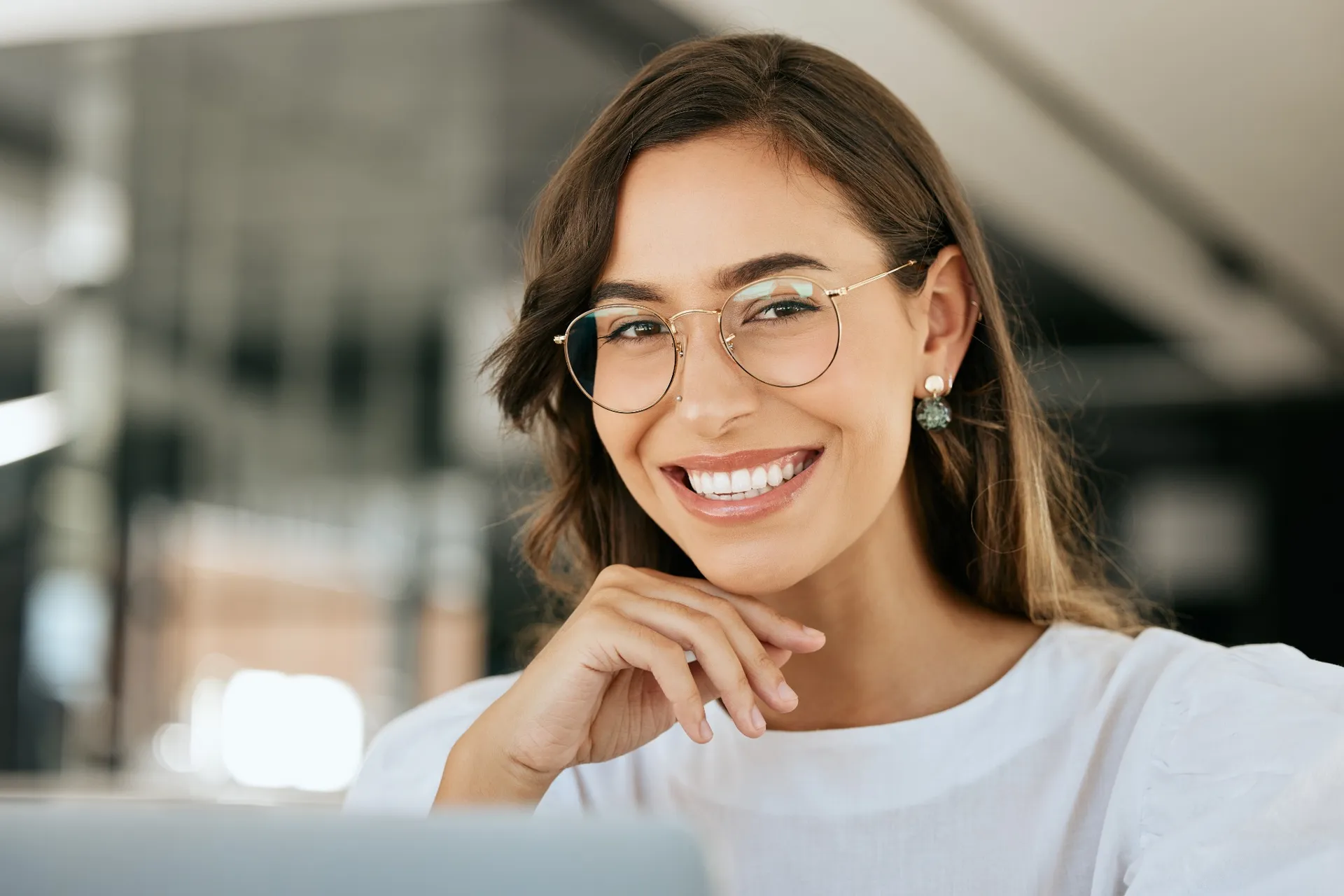 Smiling woman with glasses and clear braces, showing white teeth and resting her chin on her hand.
