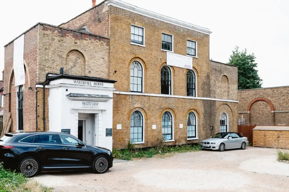 Brick building named Waterfall House with two cars parked outside on a gravel area.