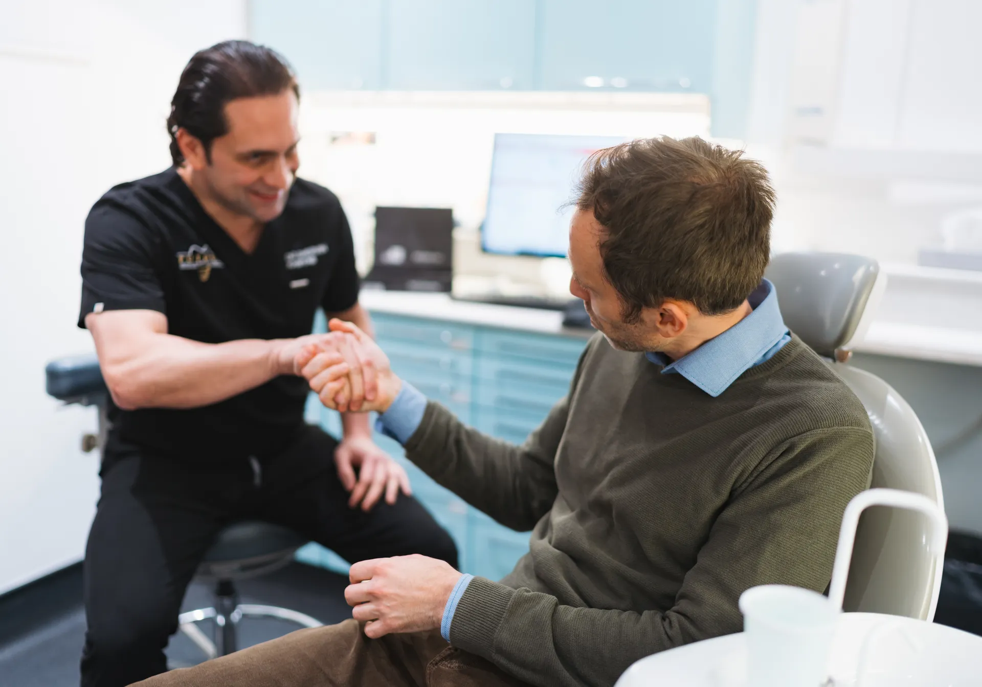 Dentist shaking hands with a male patient seated in a dental chair in a clinic.