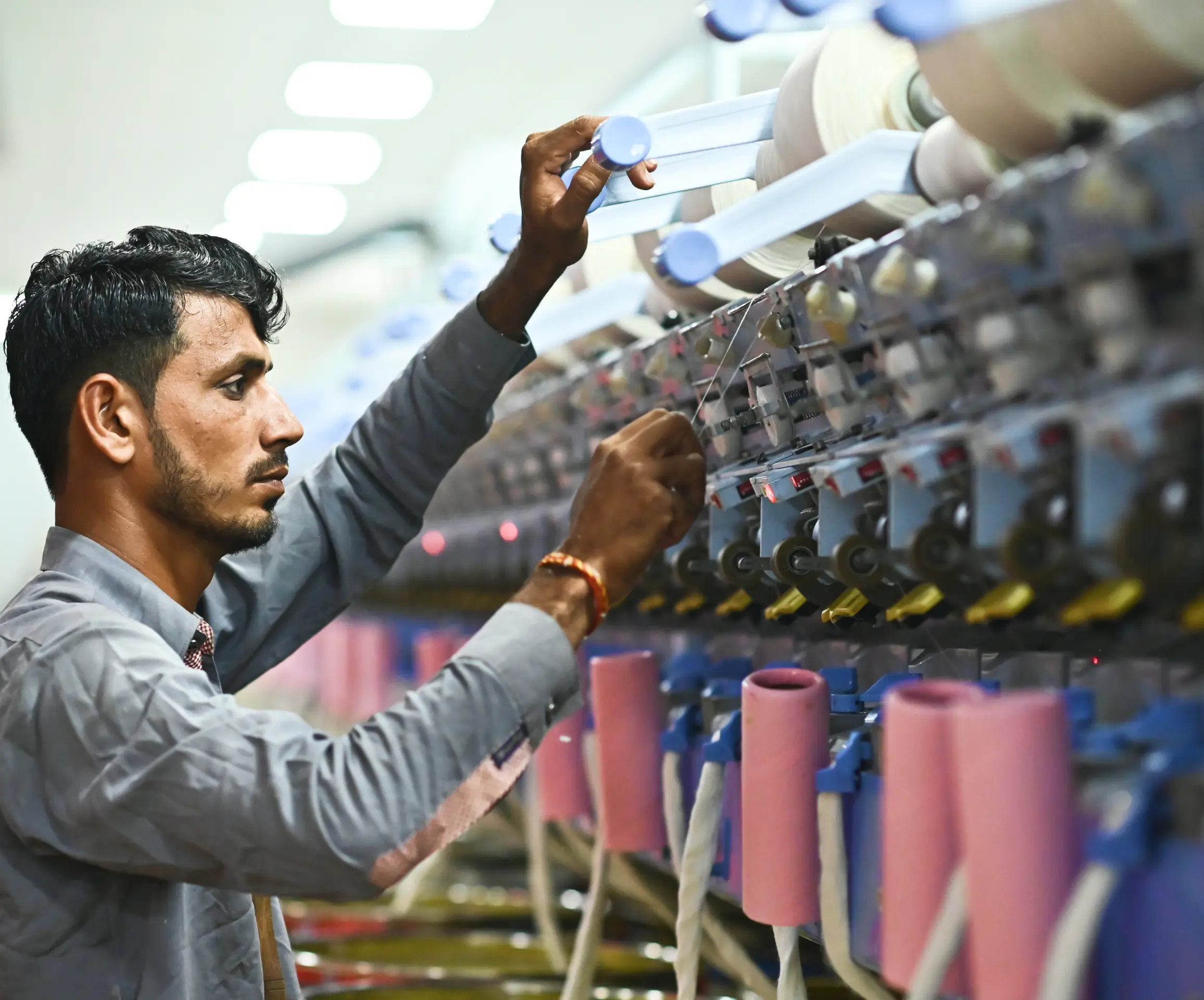 Man operating textile machinery with multiple spools of thread in a factory setting.