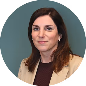 Portrait of a woman with shoulder-length brown hair wearing a beige blazer and maroon top, with a neutral expression.