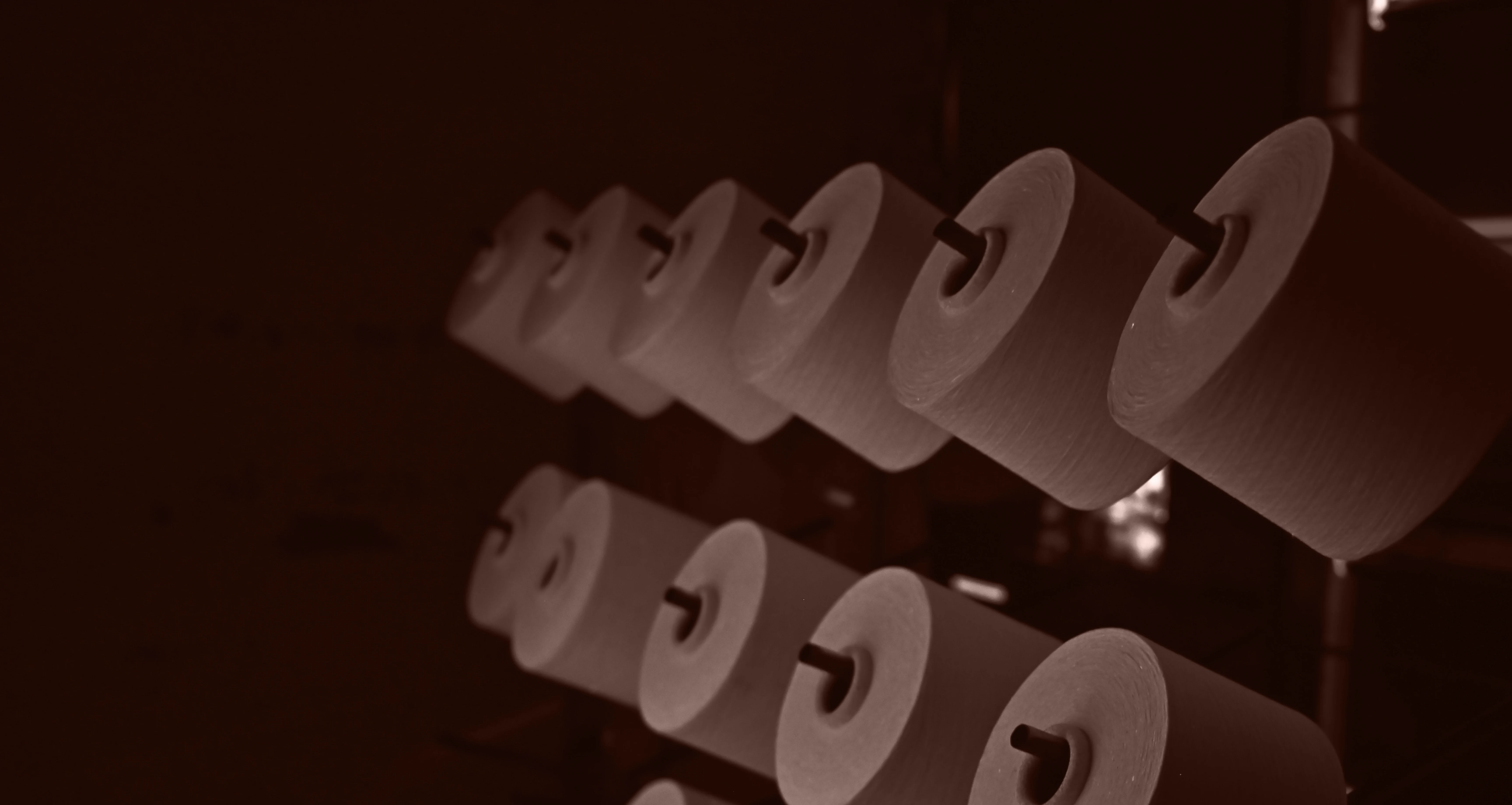 Multiple large white rolls of paper or fabric arranged on rods in a dimly lit industrial setting.