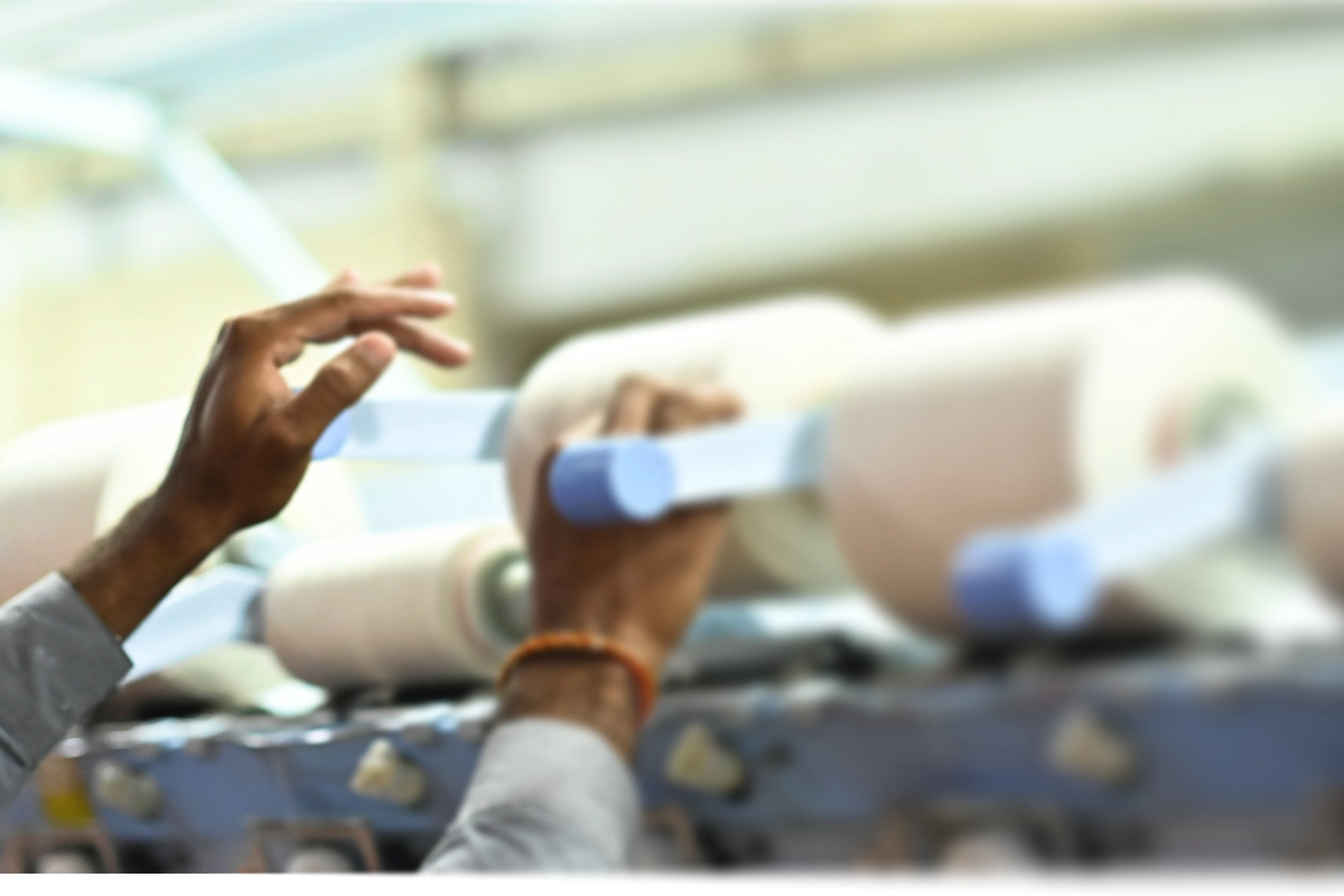 Hands adjusting cylindrical textile spools on a machine in a fabric manufacturing facility.