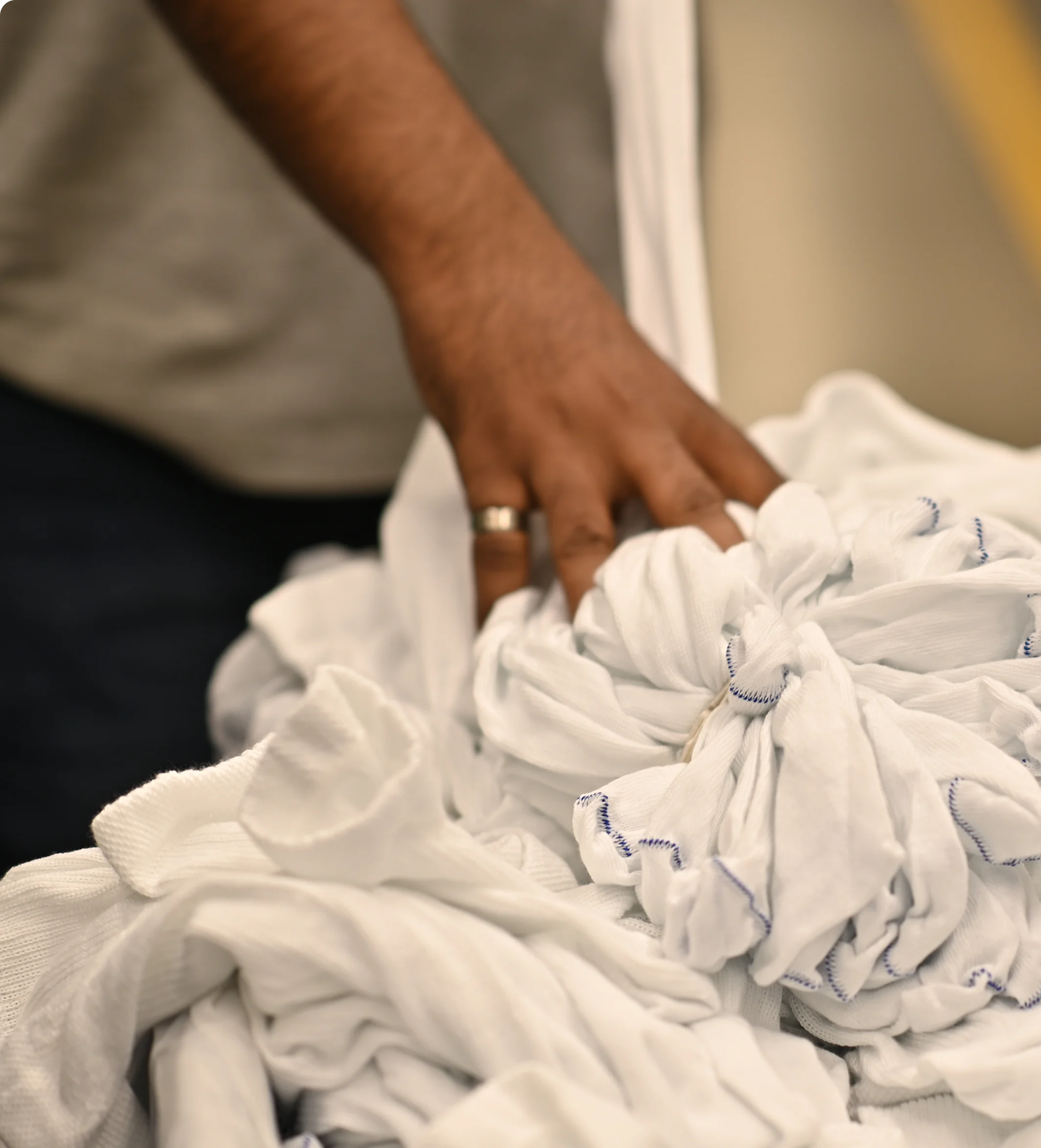 Hand with a ring touching a pile of white fabric with blue stitch edges.