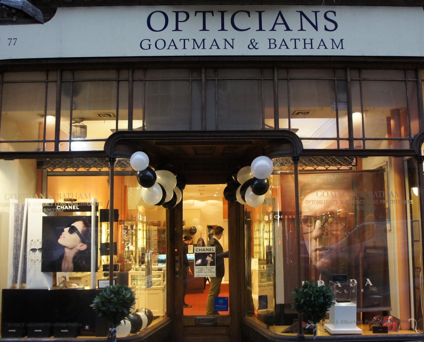 Front view of Goatman & Batham opticians store with black and white balloons around the entrance and eyewear advertisements visible inside.