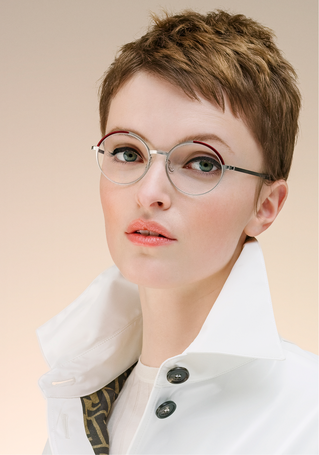 Close-up of a woman with short brown hair wearing round glasses and a white collared jacket.