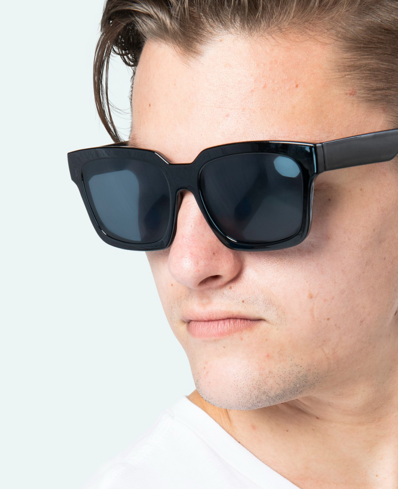 Close-up of a man wearing large black square sunglasses and a white shirt.