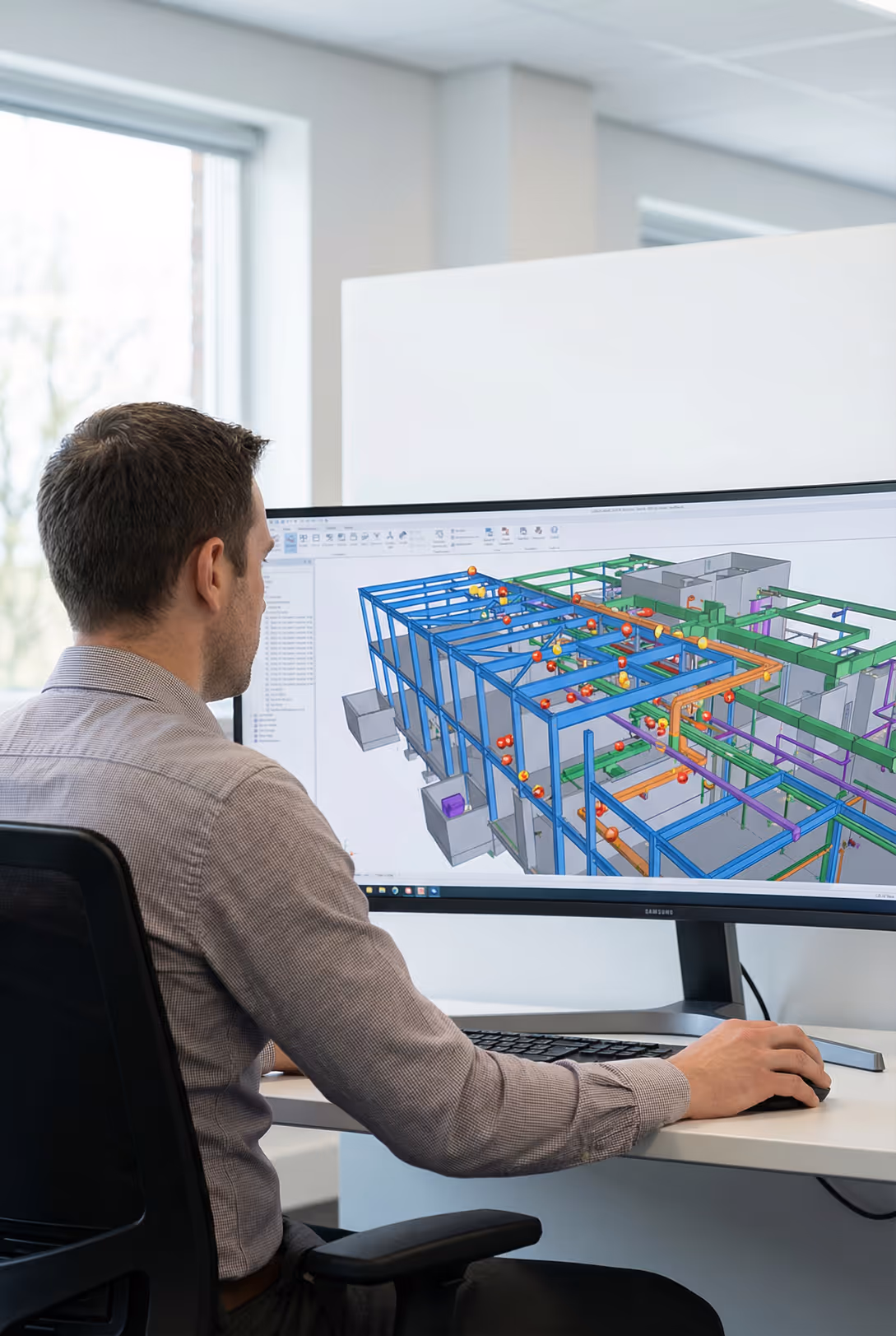 Man working on a computer with a 3D architectural model displayed on the monitor.