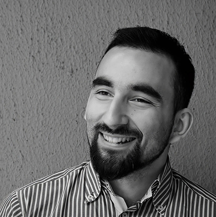 Smiling man with a beard and striped shirt against a textured wall.