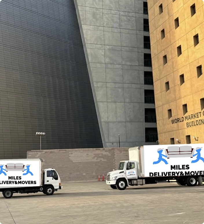 Two moving trucks with logos showing blue figures carrying a sofa and the text 'Miles Delivery & Movers' parked in front of a large building with 'World Market Center Building' sign.