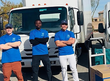 Three delivery workers in blue shirts standing with arms crossed in front of a white delivery truck.