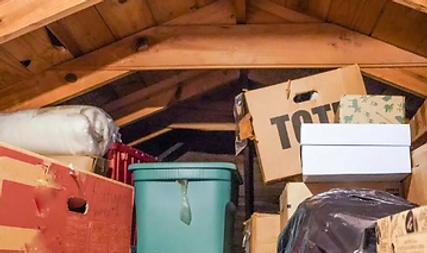 Stacked storage boxes and containers under a wooden attic roof.