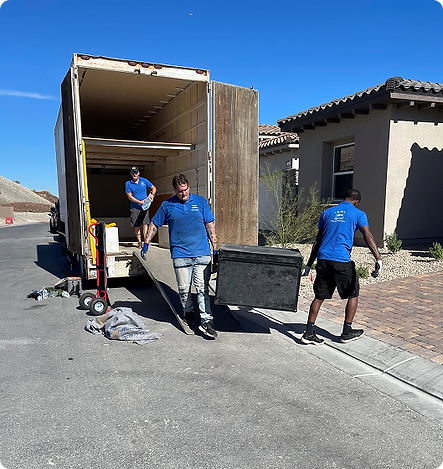 Three movers wearing blue shirts unloading a large black container from a truck in a suburban neighborhood under a clear blue sky.