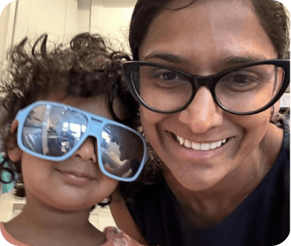 A smiling woman with glasses and a toddler with large blue sunglasses taking a close selfie.