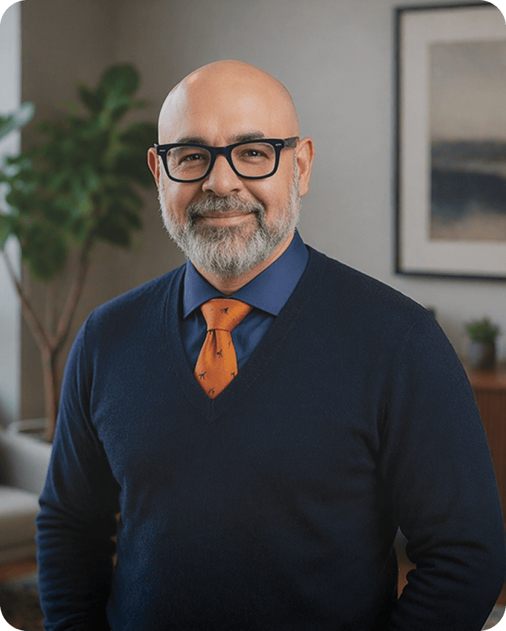 Dr Geo Espinosa smiling with glasses, a beard, and a sweater over a collared shirt and orange tie posing for a professional headshot.