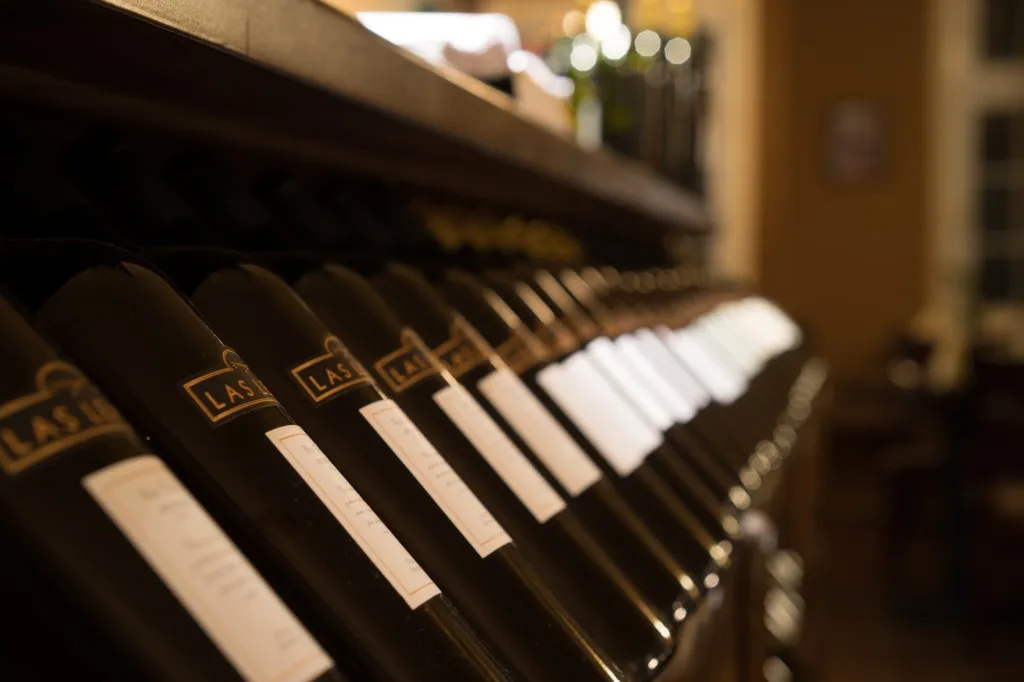 Reihe von Weinflaschen, die horizontal in einem hölzernen Regal in einem schwach beleuchteten Raum gelagert sind.