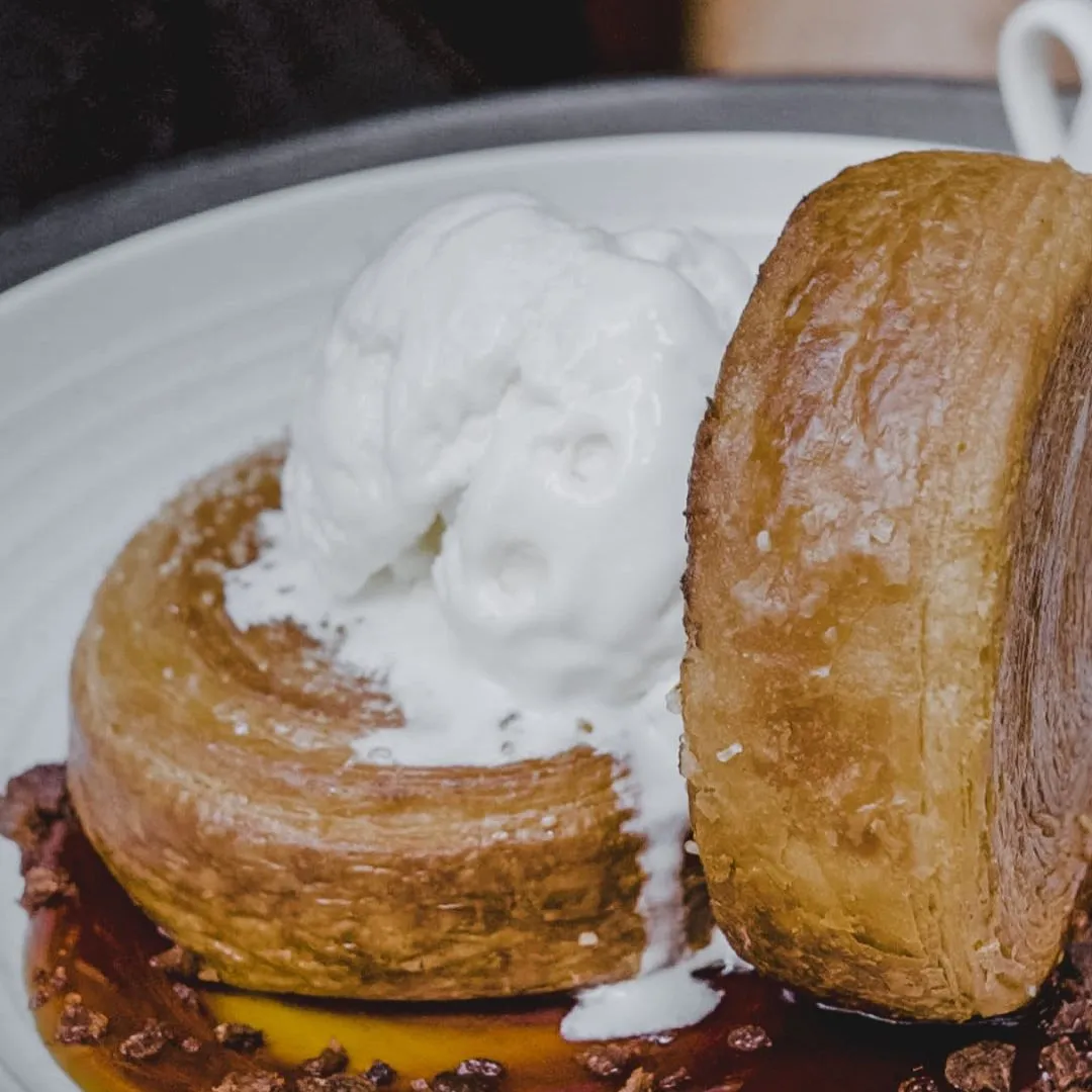 Two golden puff pastries on a white plate, one topped with a scoop of melting vanilla ice cream and drizzled with caramel sauce.