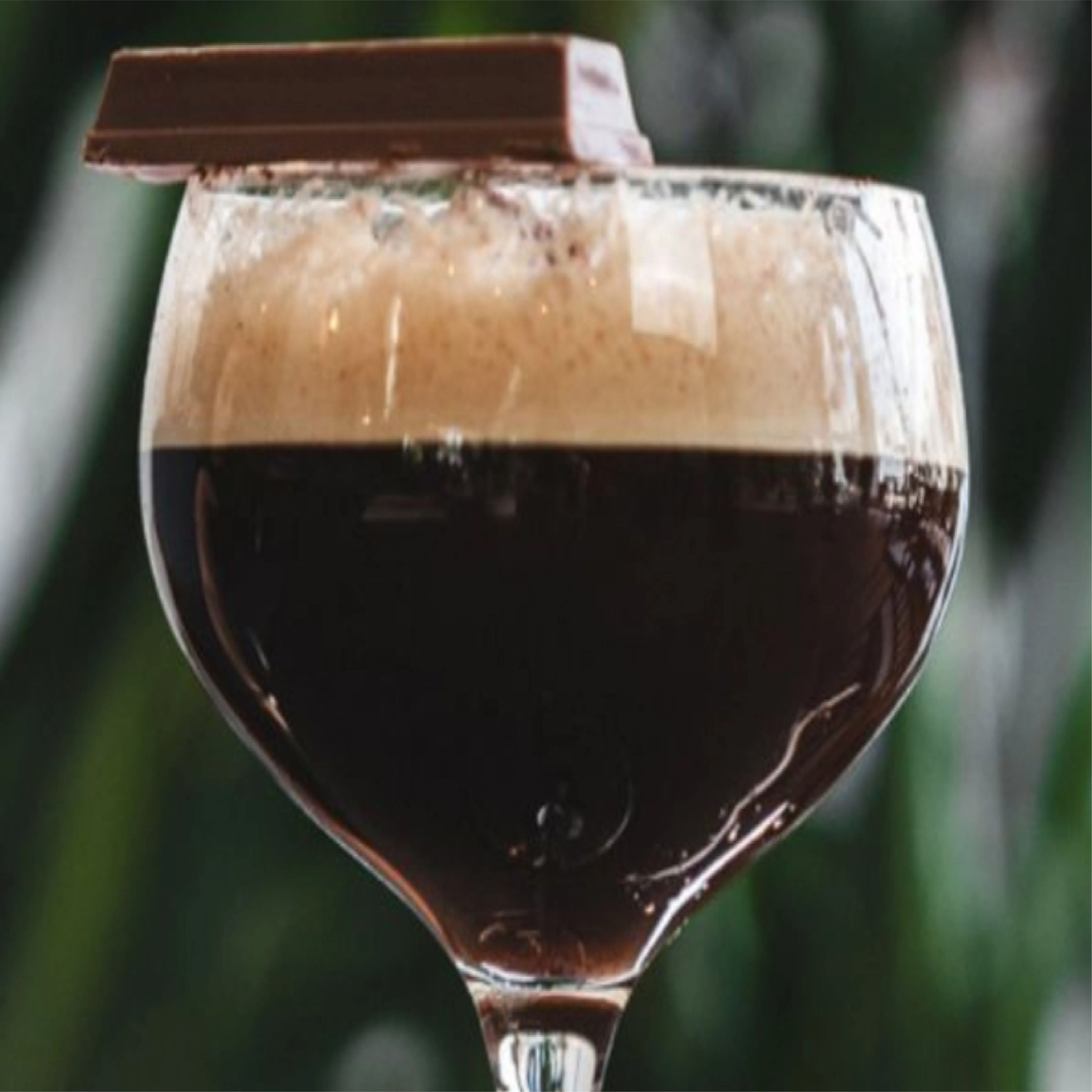 Glass of dark stout beer with creamy foam topped with a square of chocolate.