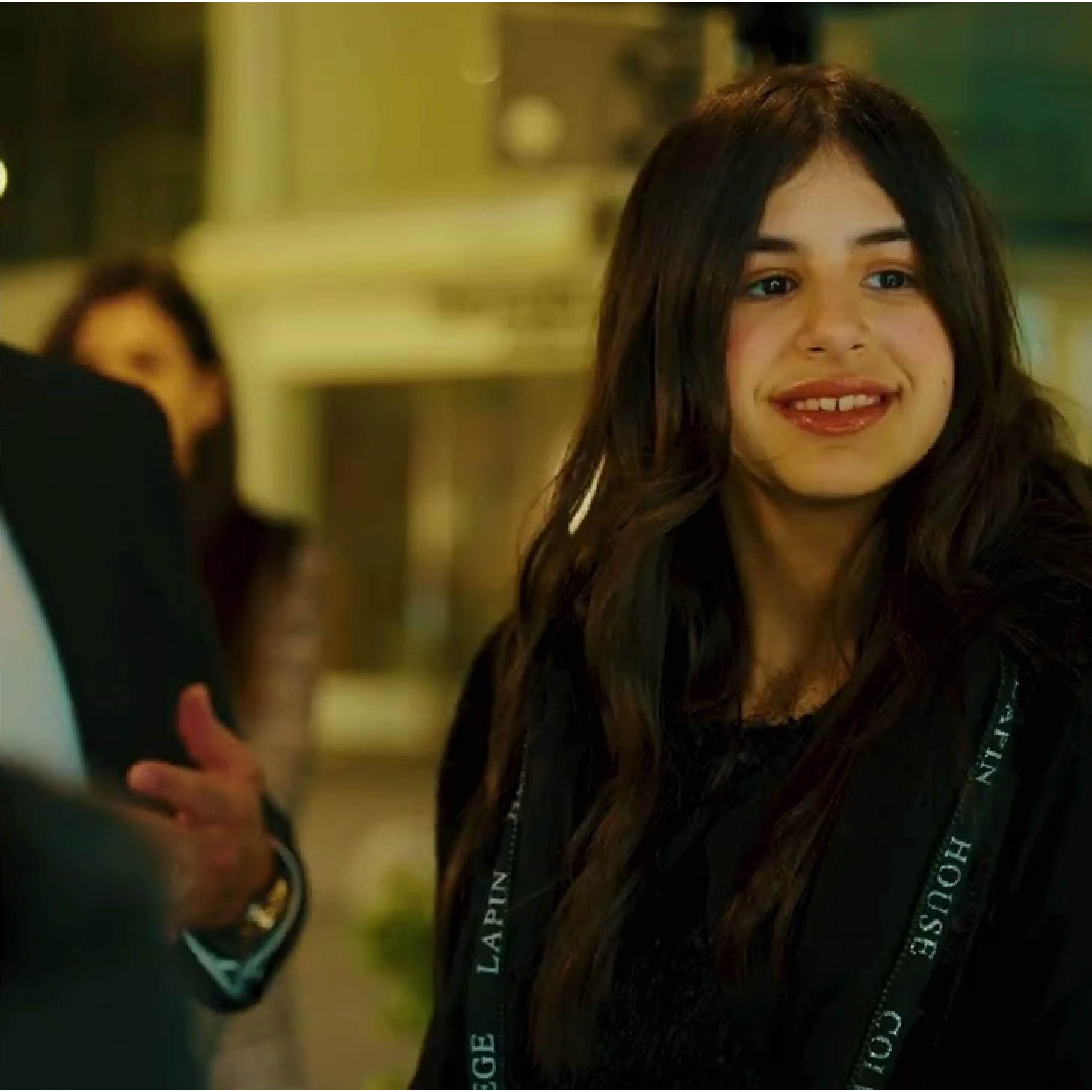 Young woman with long dark hair smiling and looking to the side in an indoor setting.