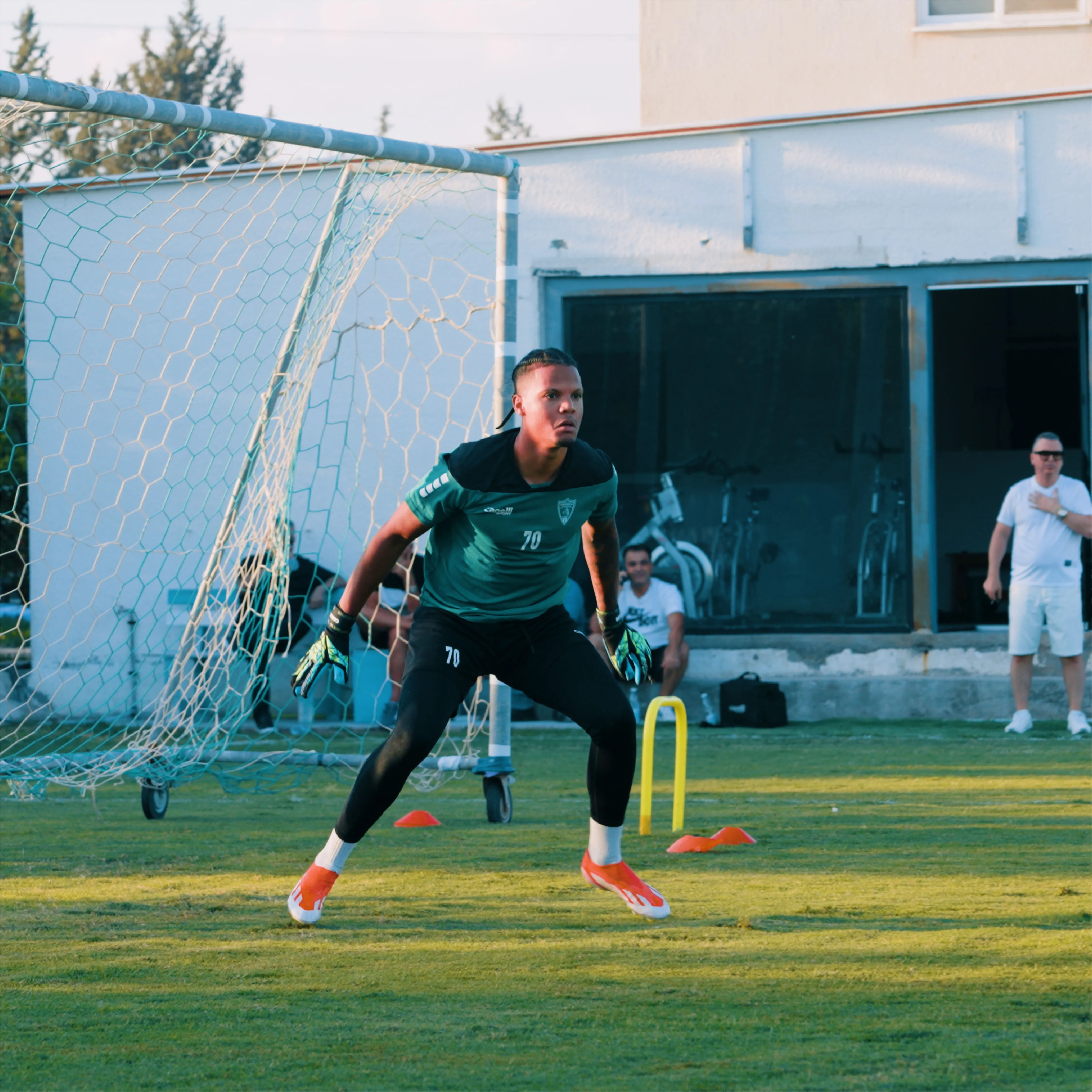 Soccer goalkeeper in green and black training gear focused and ready in front of the goal on a grass field during practice.