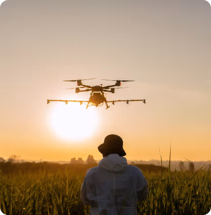 Person operating a drone flying over a grassy field at sunset.