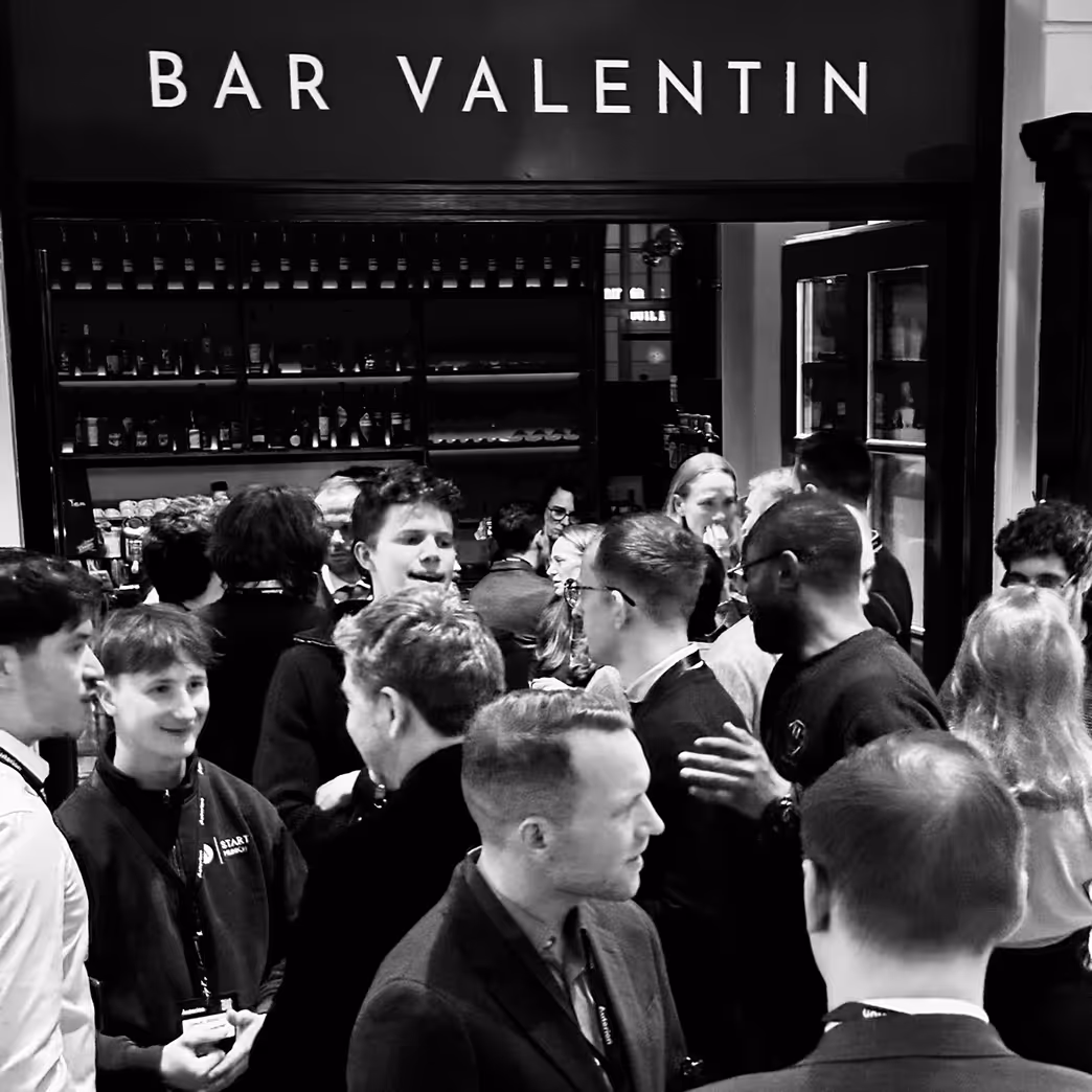 Crowd of people socializing inside Bar Valentin with shelves of bottles in the background.