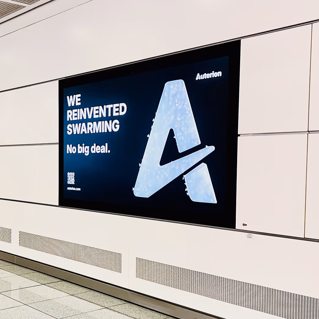 Digital wall advertisement with text 'WE REINVENTED SWARMING No big deal.' and a large stylized letter A with the brand name Auterion.