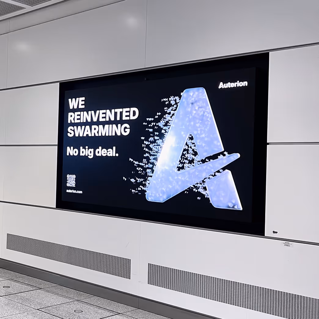 Digital display in a subway station with text 'WE REINVENTED SWARMING No big deal.' beside a large stylized letter A made of small blue triangles, with 'Auterion' logo in top right corner.