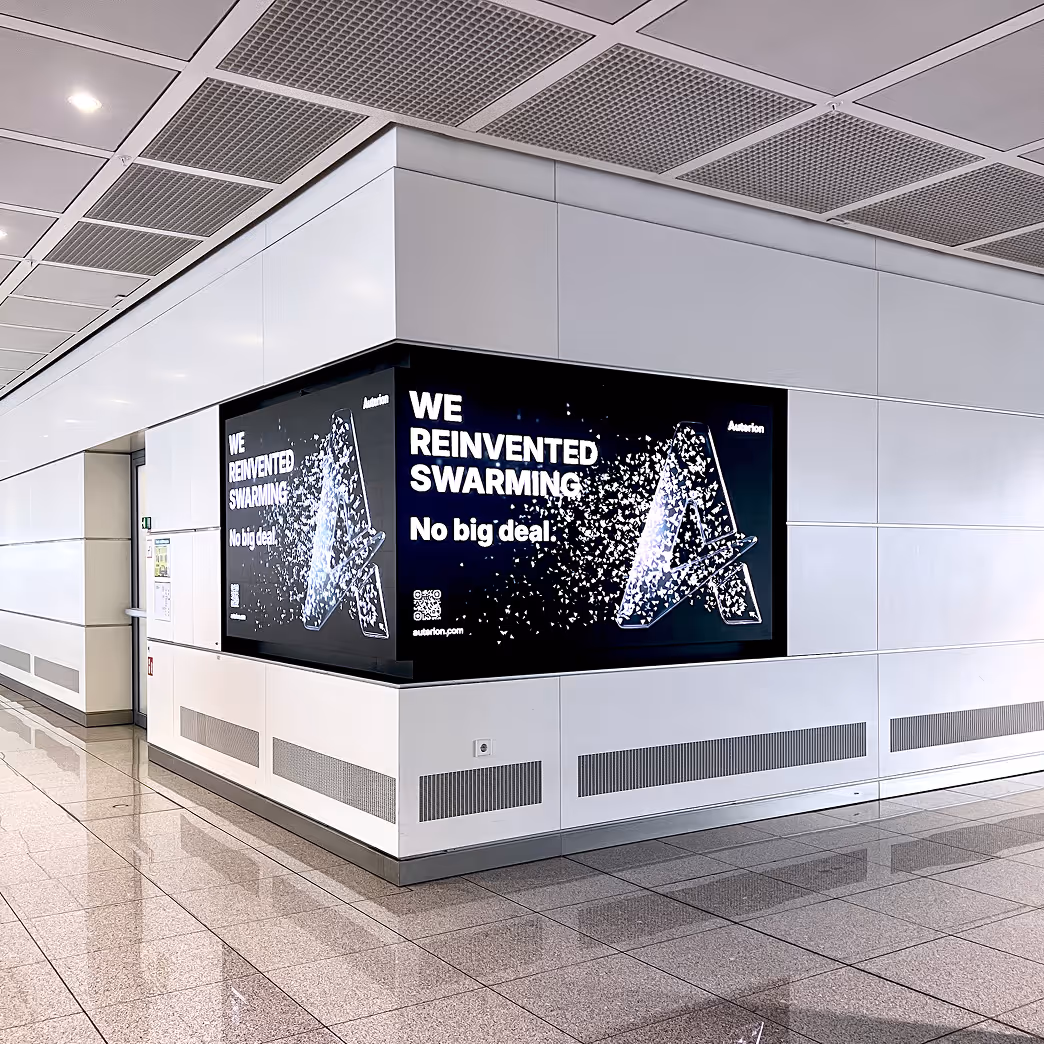 Corner digital advertisement in a hallway displaying the text 'WE REINVENTED SWARMING No big deal' with a fragmented letter A graphic.
