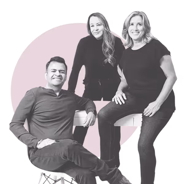 Three adults posing together, one seated and two standing behind a bench, against a pale pink circular background.