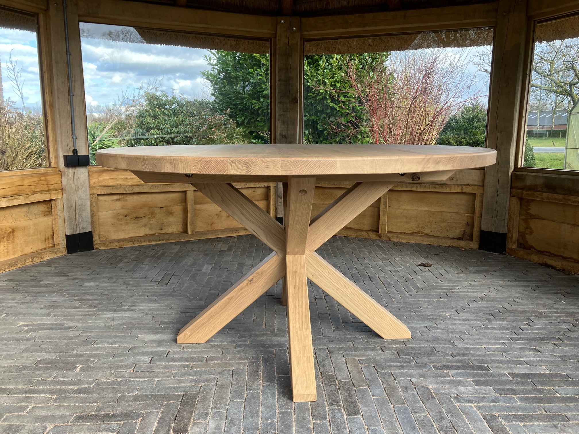 Ronde maatwerk eettafel met kruispoot, geplaatst in een tuinprieel