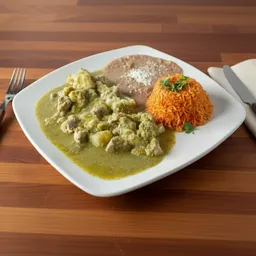 Plate with green chile verde stew, refried beans, and Mexican red rice garnished with cilantro on a wooden table.