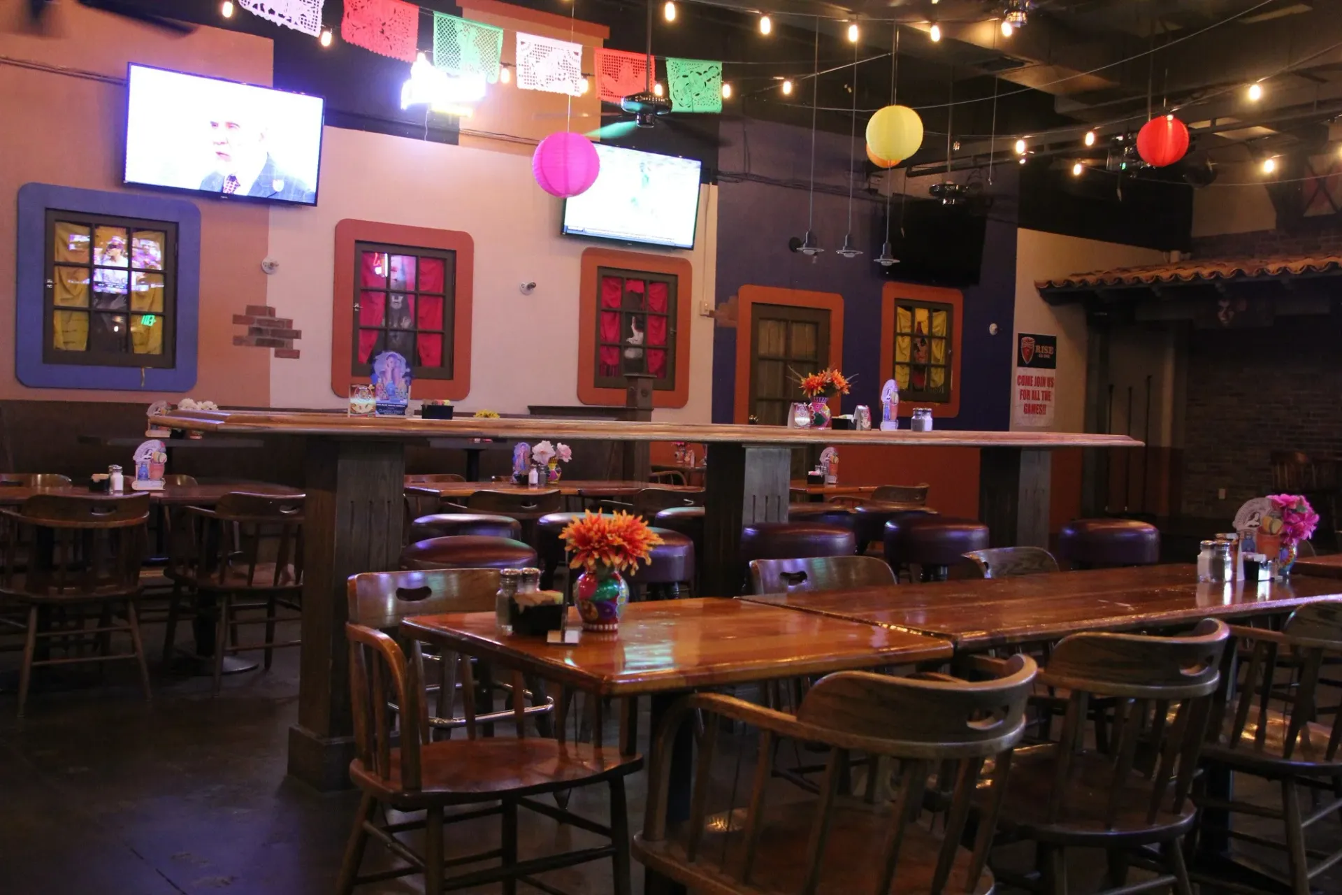 Interior of a cozy restaurant with wooden tables and chairs, colorful hanging lanterns, and festive papel picado decorations.
