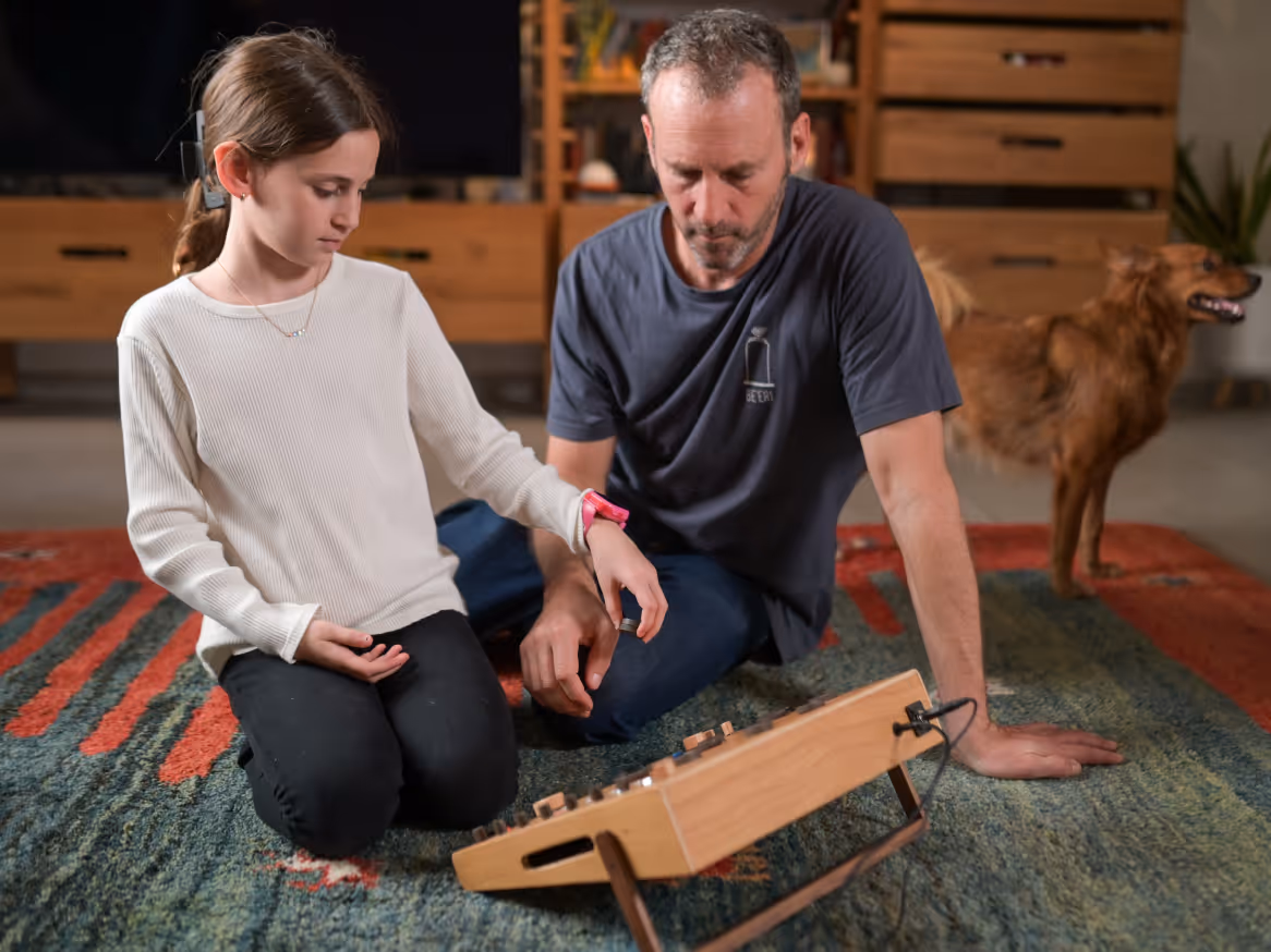 Person adjusting knobs on a Tembo wooden electronic musical instrument with round buttons on a carpeted floor.