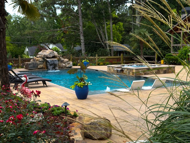 Freeform swimming pool with rock waterfall and raised stone spa on a paver patio