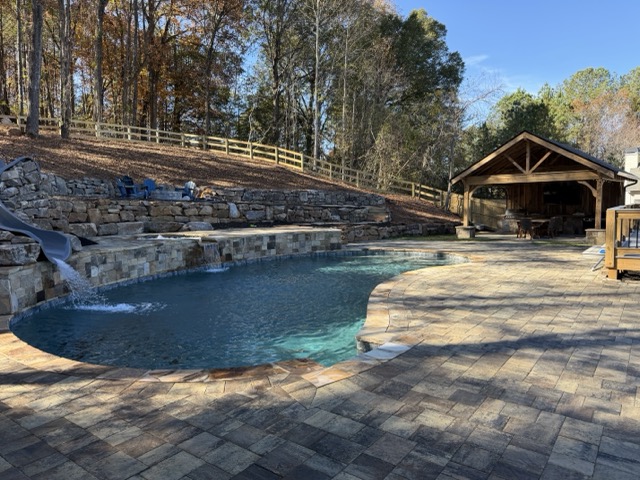 Freeform swimming pool with rock waterfall and raised stone spa on a paver patio