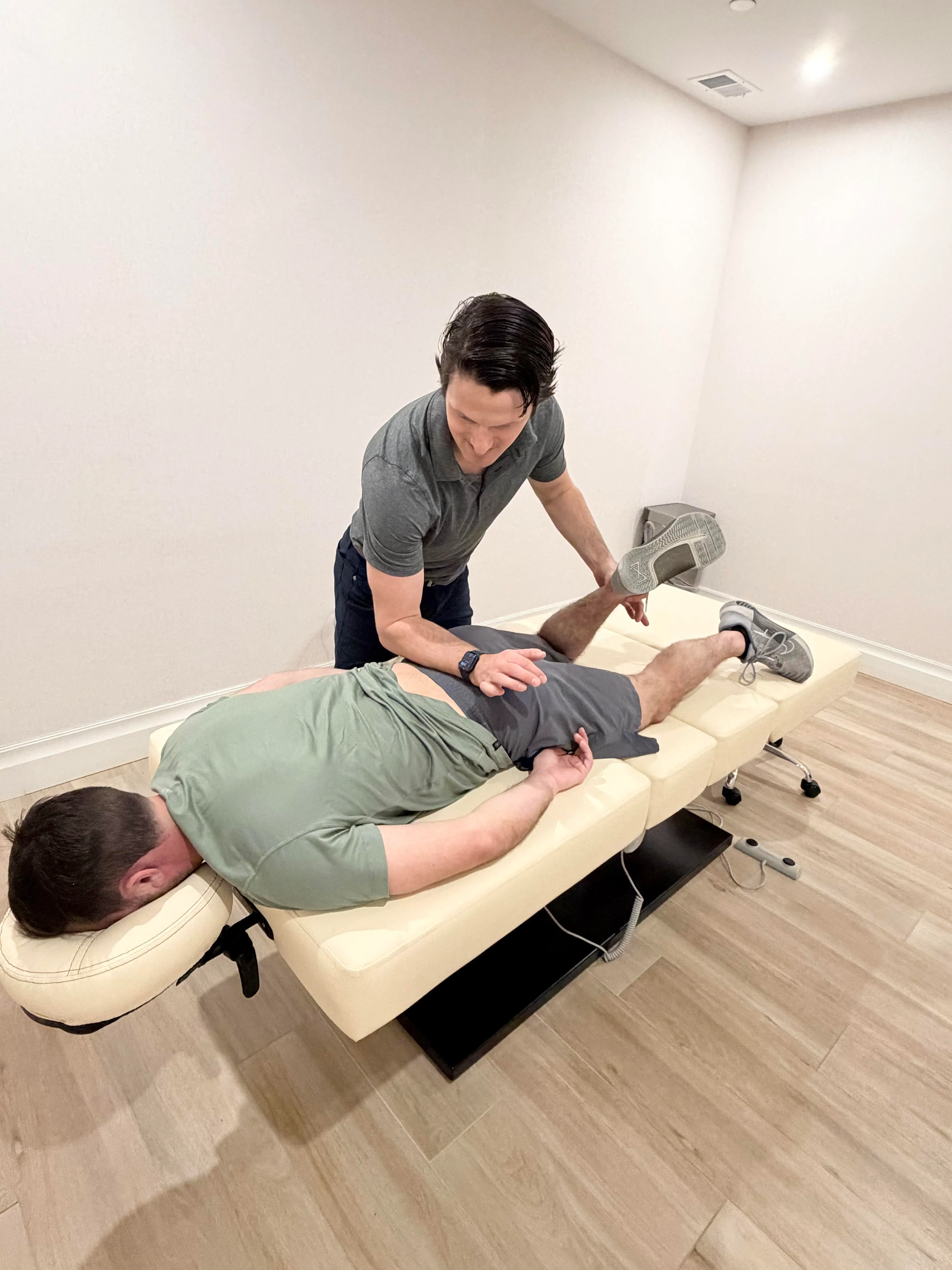 Physical therapist performing hip external rotation mobilization on a man lying face down on an examination table.