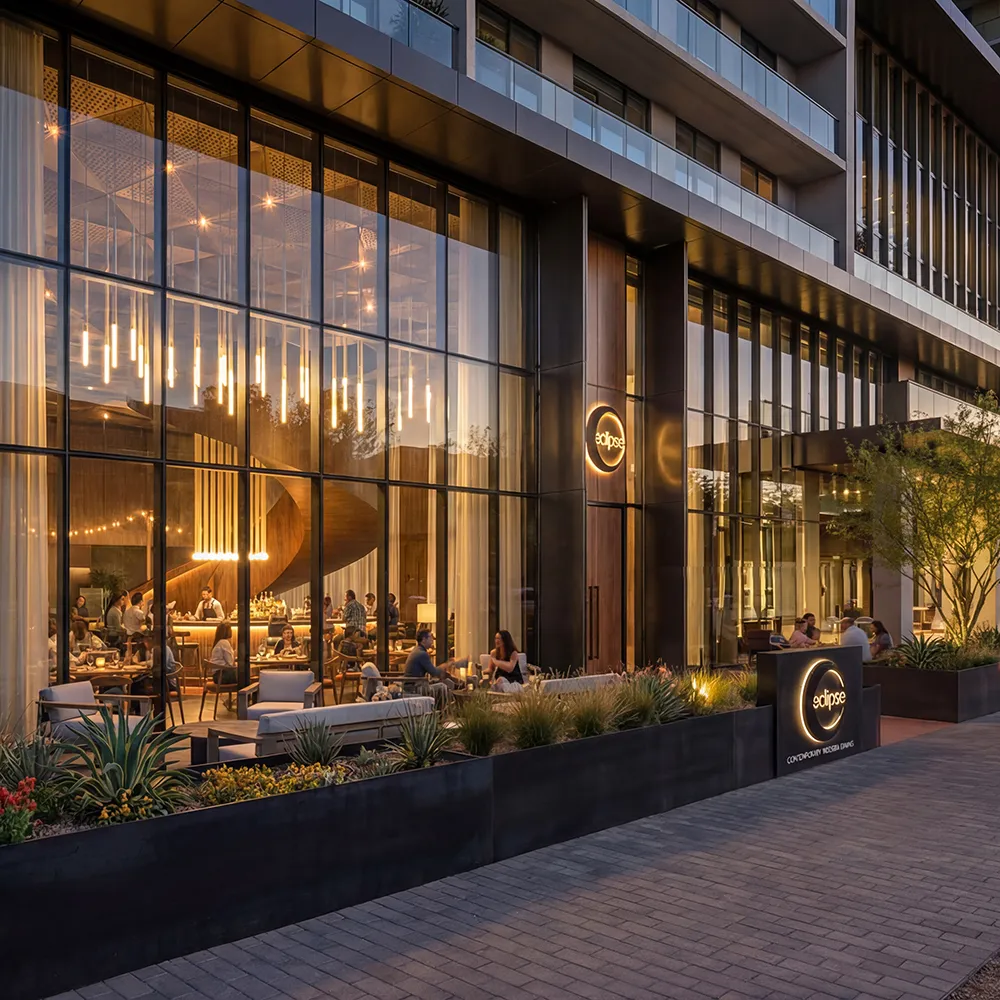 Modern restaurant with large glass windows, warm lighting, outdoor seating, and people dining at sunset.