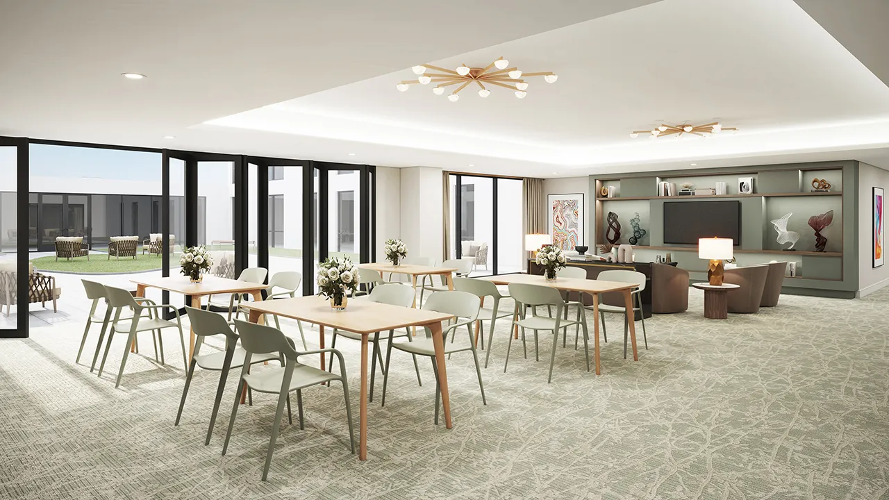 Bright activity room with tables, chairs, flower vases, large windows, and a TV with seating area.