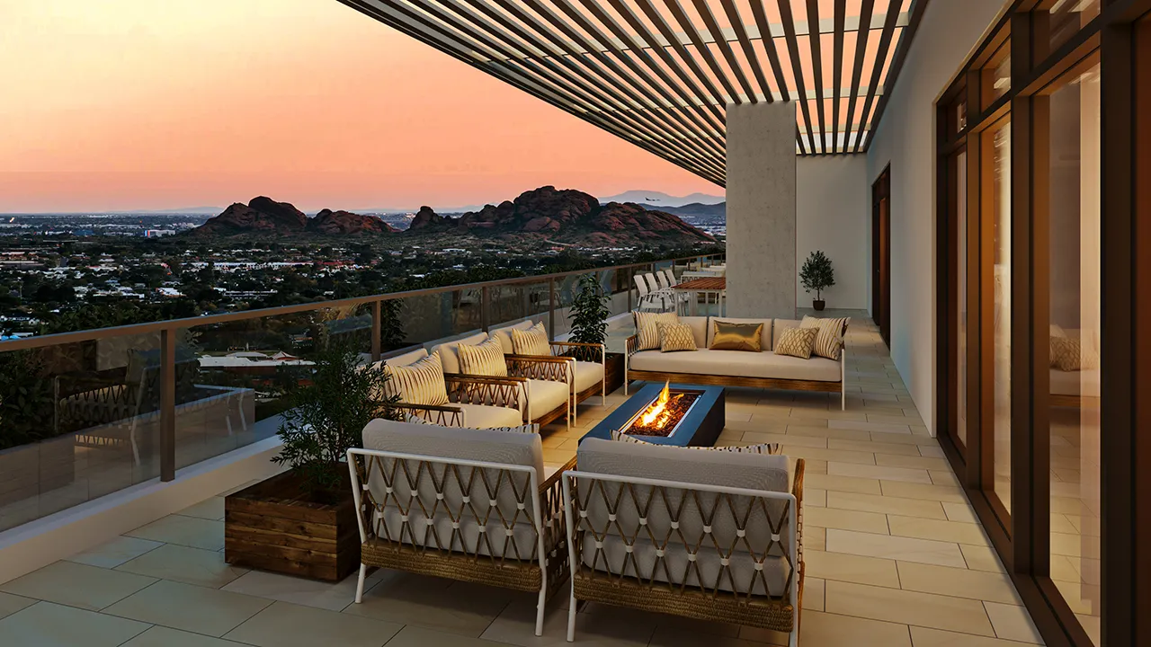 Sunset view from a balcony with cushioned chairs around a fire pit and mountains in the distance.