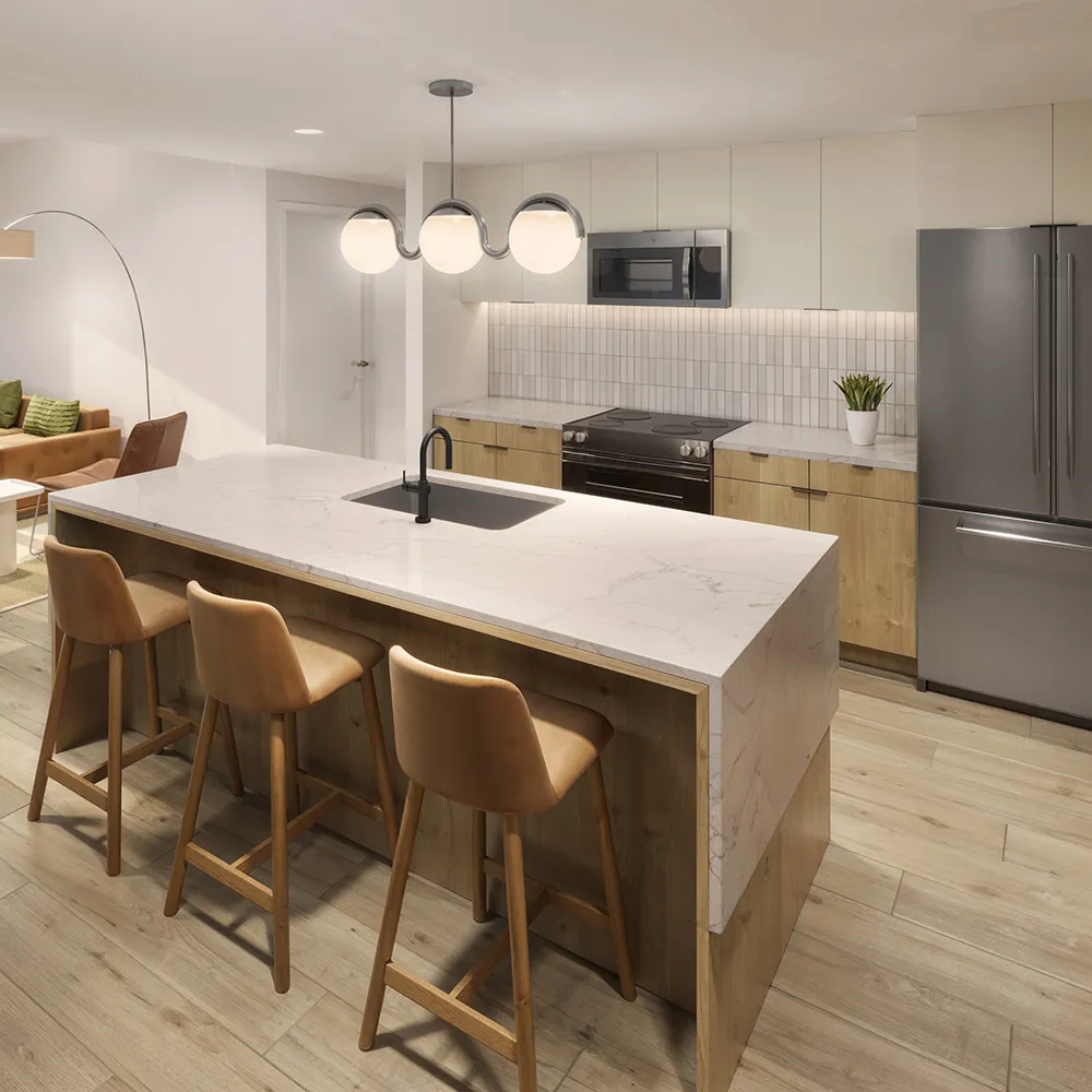Modern kitchen with marble island, three leather stools, stainless appliances, and wood cabinets.