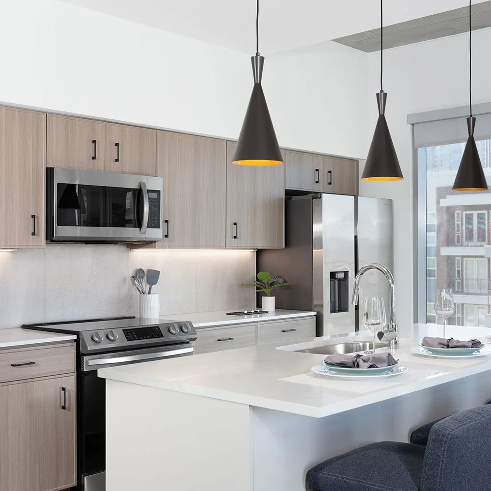 Modern kitchen with light wood cabinets, stainless appliances, island with sink and three dark chairs.