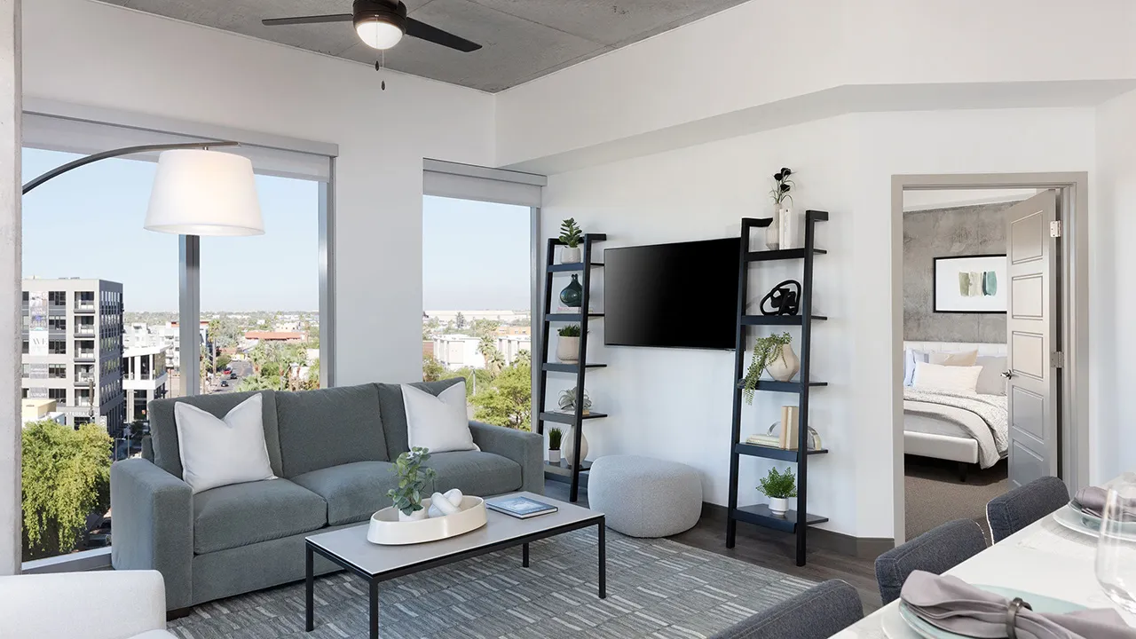 Modern living room with gray sofa, coffee table, flat-screen TV, decor shelves, and view of bedroom.