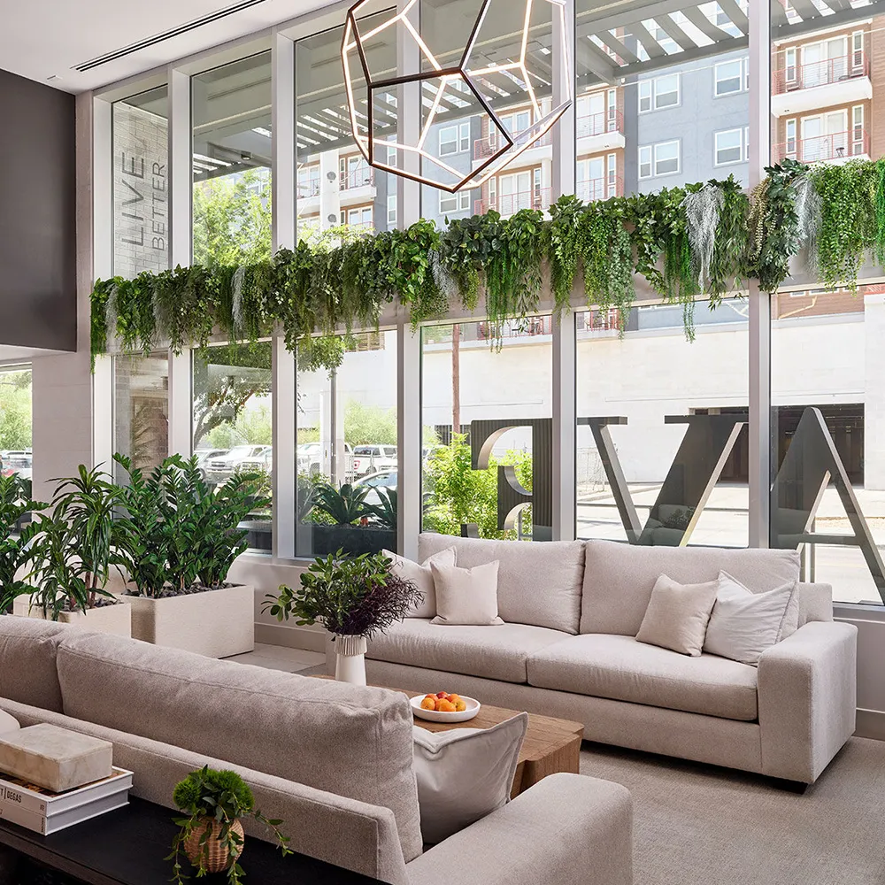Modern lobby with large windows, green plants, light sofas, and tables with chairs.