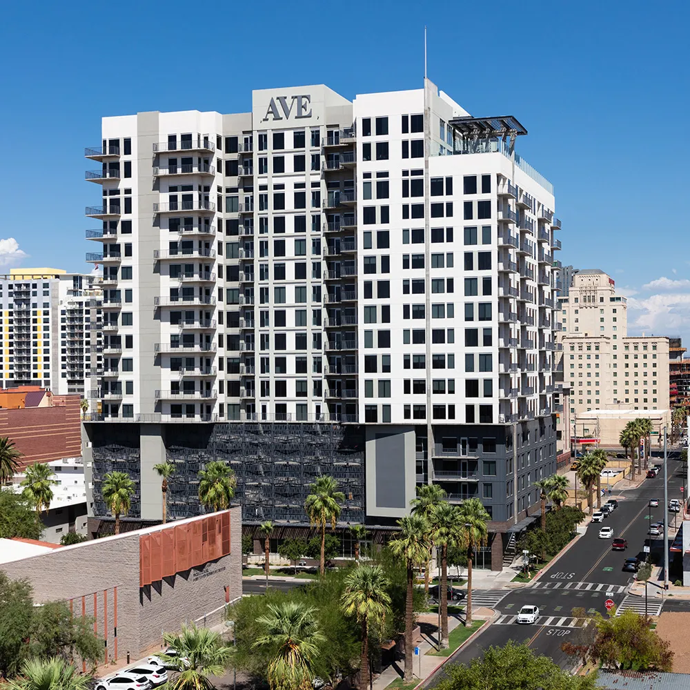 Day view of AVE apartment building lit up in Downtown Phoenix with surrounding buildings and clear sky.