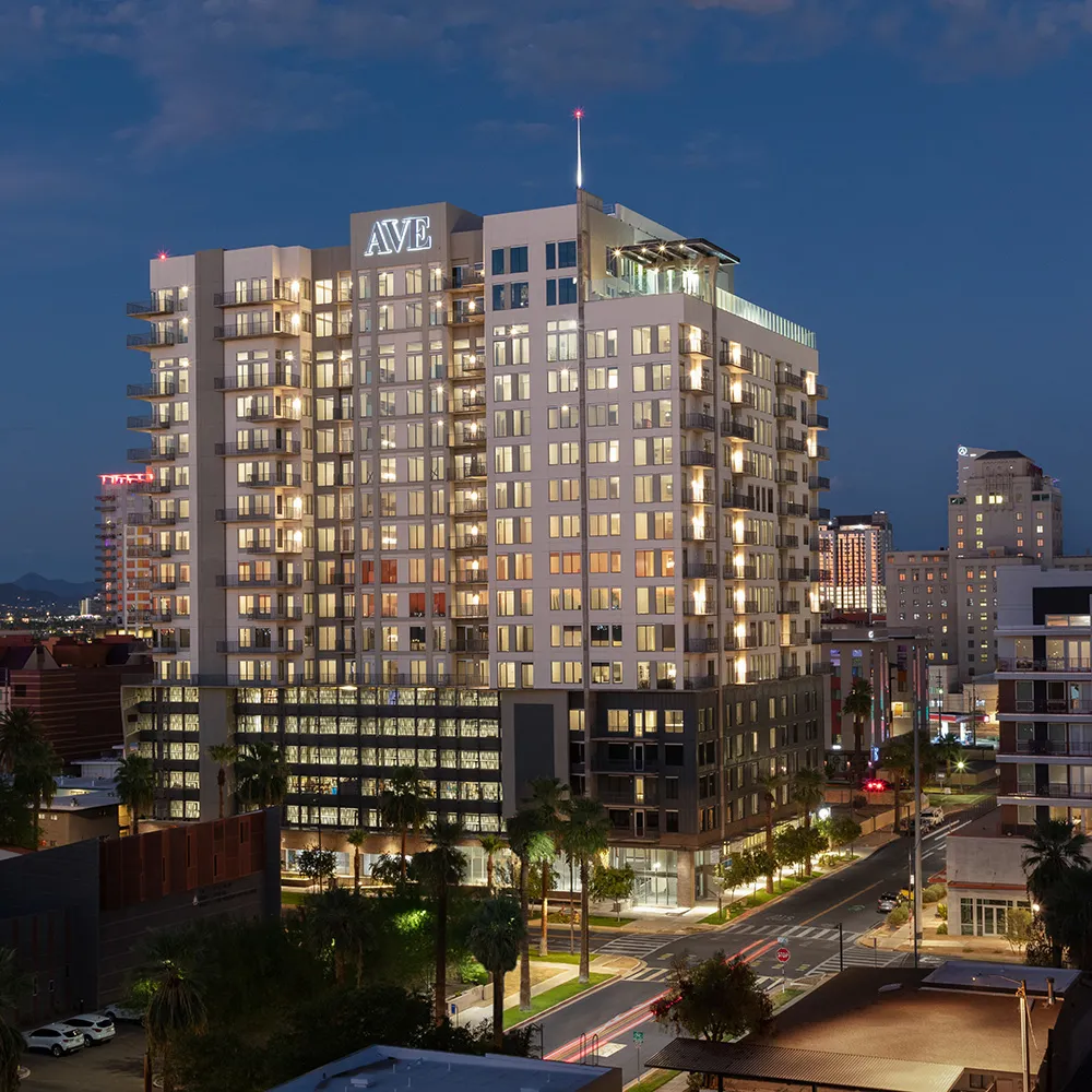 Night view of AVE apartment building lit up in Downtown Phoenix with surrounding buildings and clear sky.