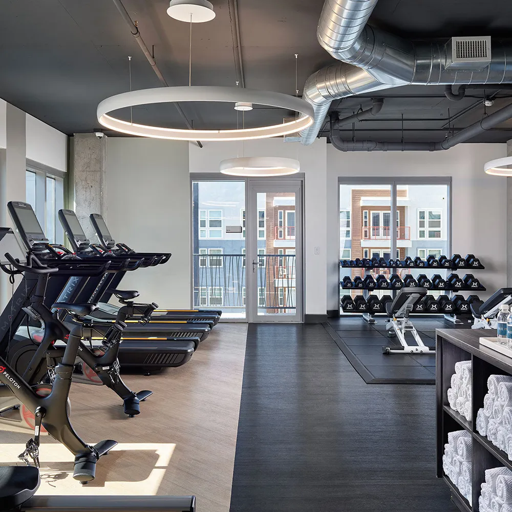Modern gym with exercise bikes, treadmills, dumbbells rack, benches, rolled towels, and water bottles.