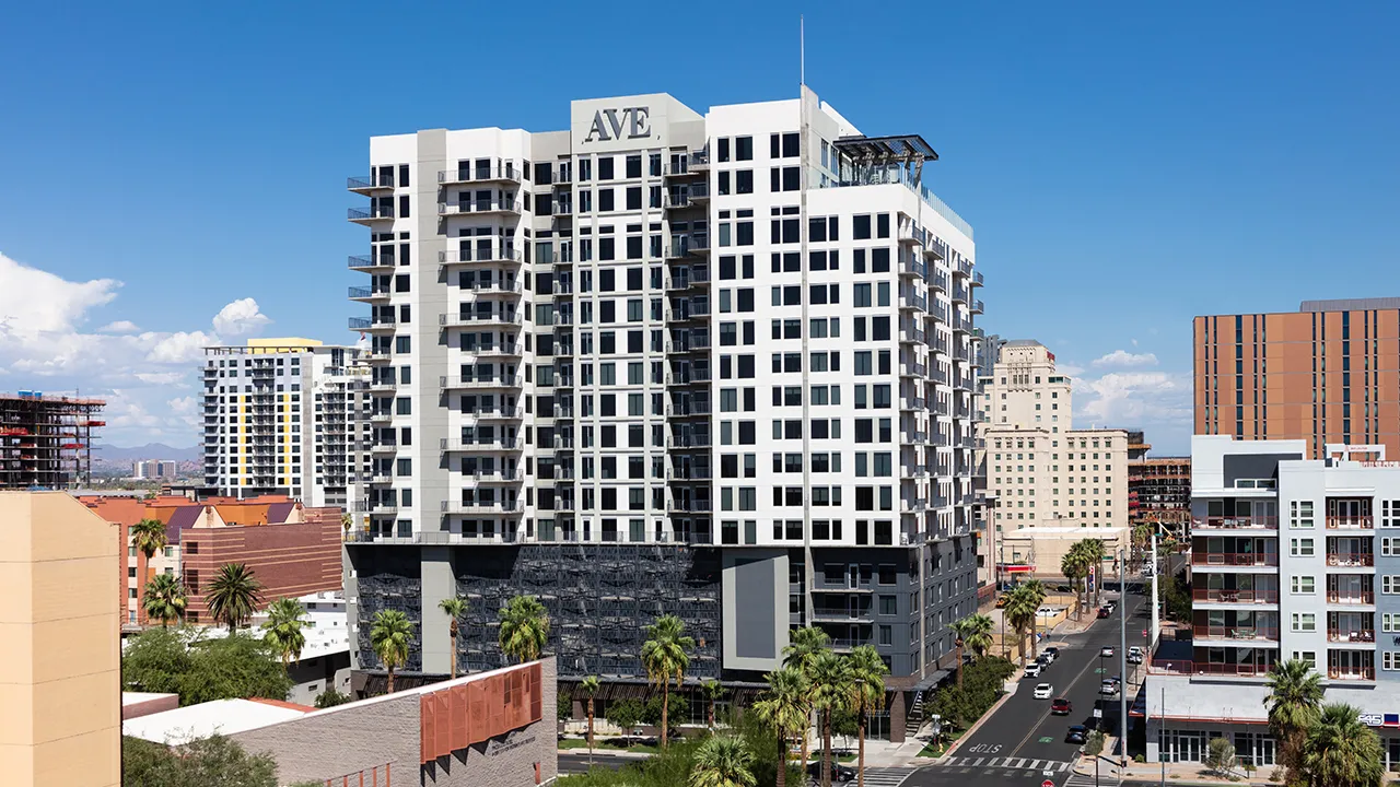 Day view of AVE apartment building lit up in Downtown Phoenix with surrounding buildings and clear sky.