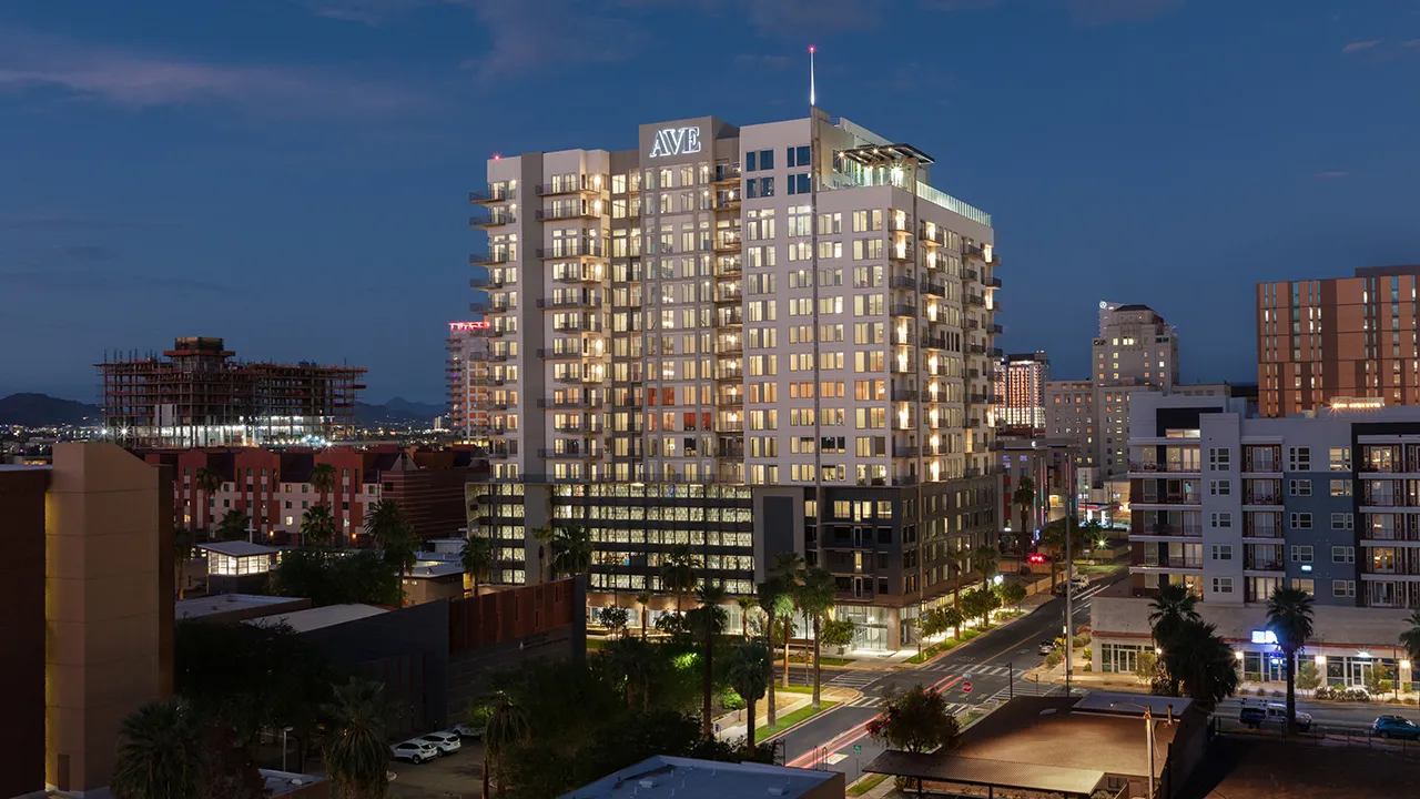 Night view of AVE apartment building lit up in Downtown Phoenix with surrounding buildings and clear sky.